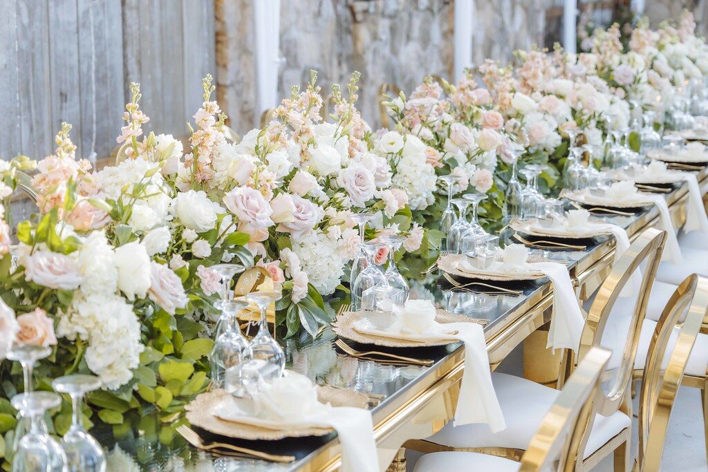 Long reception table dressed with white flowers and gold chairs